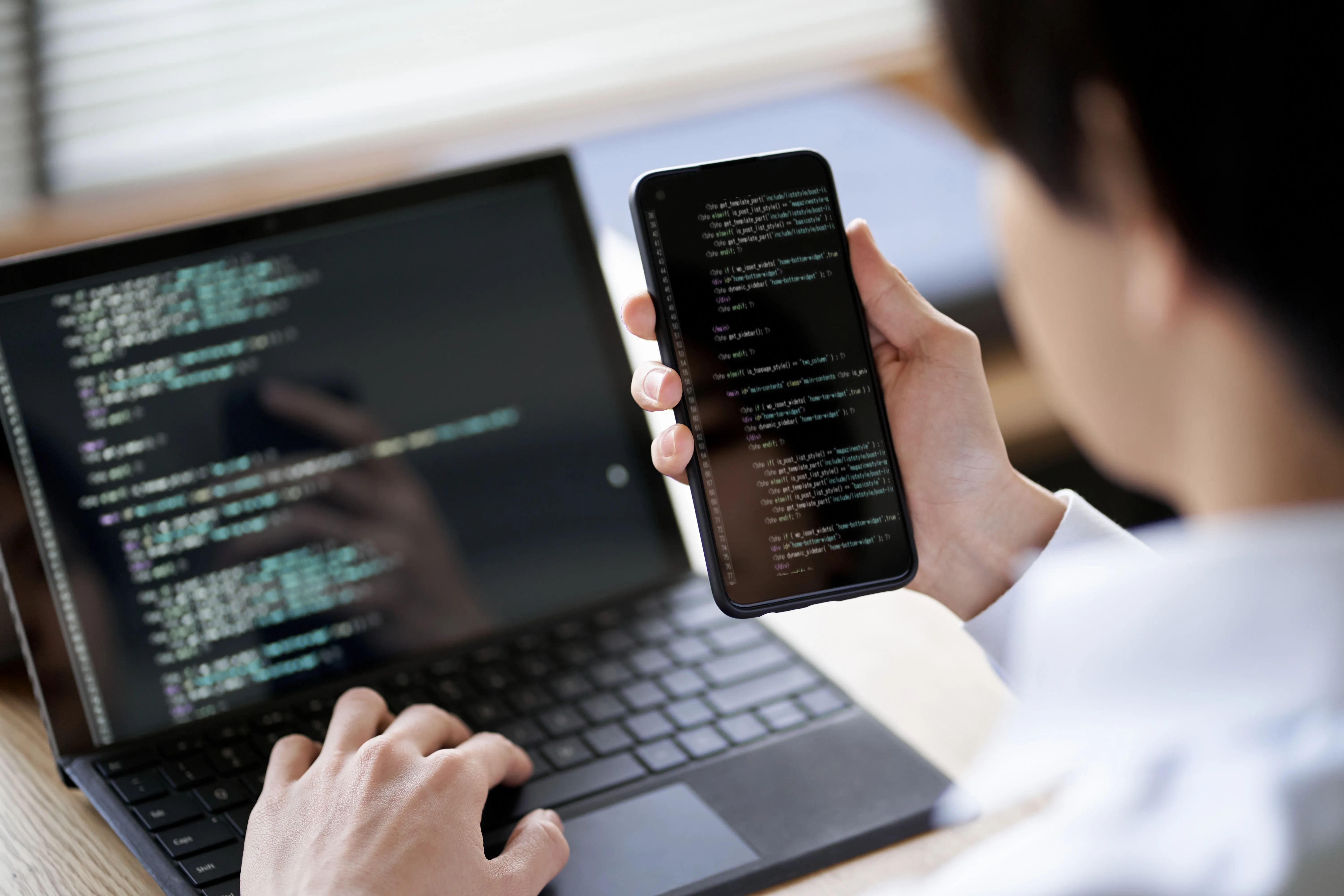 Développeur qui contrôle son code entre son telephone et son ordinateur